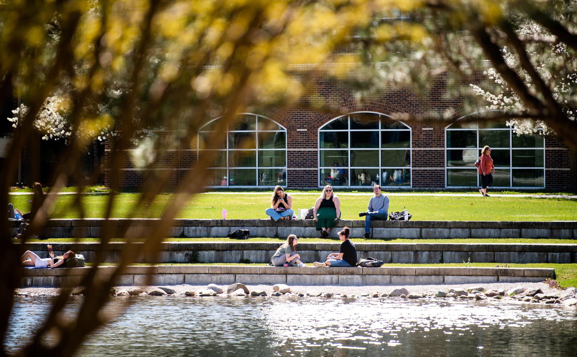Students sitting in front of Zumberge Pond behind the Kirkhof Center
